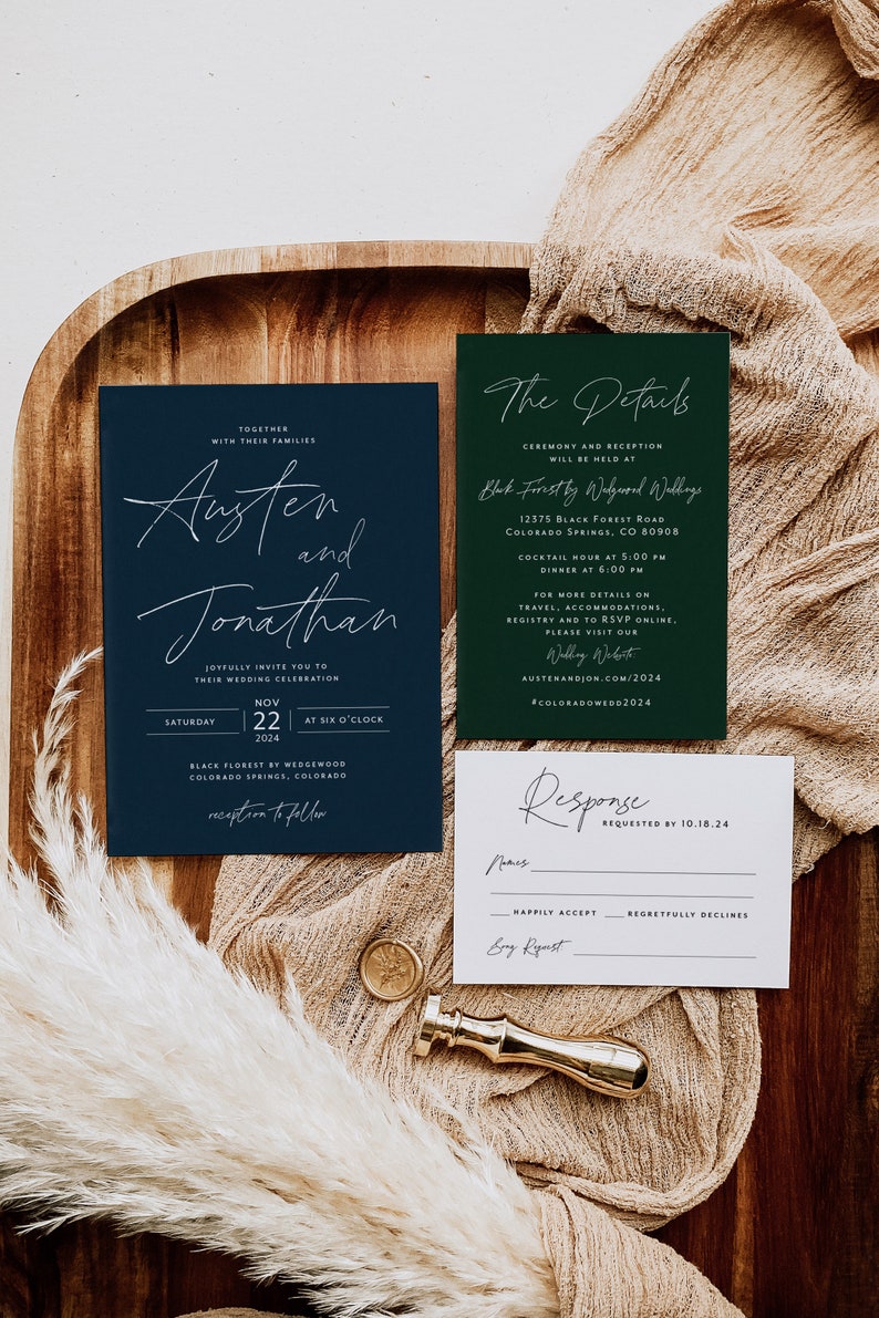 May include: A navy blue and green wedding invitation suite with white calligraphy. The invitation card features the names Austen and Jonathan, the date November 22, 2024, and the location Black Forest by Wedgewood, Colorado Springs, Colorado. The details card includes the ceremony and reception location, date, time, and website address. The response card has a space for the guest's name, RSVP options, and a space for a song request.