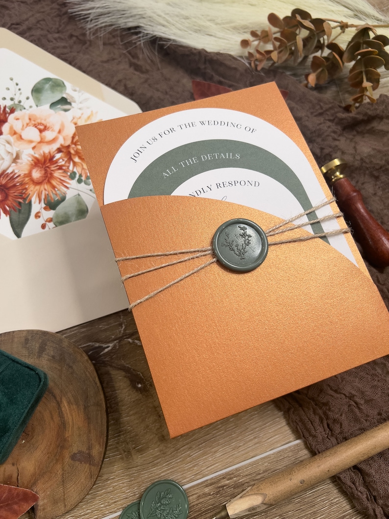 Puede incluir: Una invitaci&oacute;n de boda de color cobre con un bolsillo interior verde y blanco. La invitaci&oacute;n tiene un sello de cera con un dise&ntilde;o floral y el texto "Join us for the wedding of" y "All the details" en el frente.