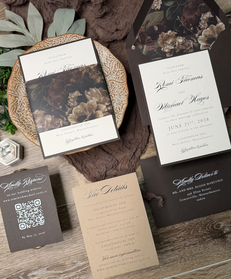 May include: A wedding invitation suite featuring cream-colored cards with dark brown text and floral envelope liners. The set includes a main invitation, a details card, an RSVP card with a QR code, and a dark brown envelope with floral interior.