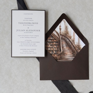 Theodora wedding invitation featuring a cream invitation with refined serif typography beside a dark brown A7 envelope opened to reveal a dramatic vintage library staircase liner, styled with black sheer ribbon.