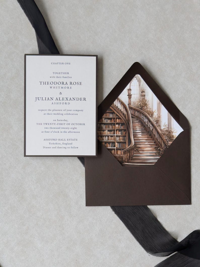Theodora wedding invitation featuring a cream invitation with refined serif typography beside a dark brown A7 envelope opened to reveal a dramatic vintage library staircase liner, styled with black sheer ribbon.