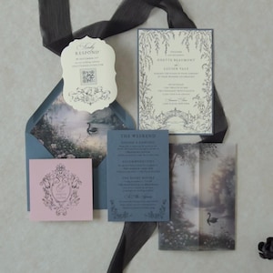 Dreamy blue fairytale wedding invitation suite featuring ivory botanical invitation, Marina blue details card, Cloud Ivory scalloped RSVP, Dusk pink tag, and matching blue envelope with a misty swan lake illustration inside.