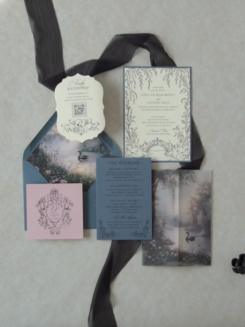 Dreamy blue fairytale wedding invitation suite featuring ivory botanical invitation, Marina blue details card, Cloud Ivory scalloped RSVP, Dusk pink tag, and matching blue envelope with a misty swan lake illustration inside.