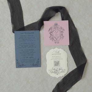 Romantic swan lake wedding stationery with an open Marina blue envelope revealing a dreamy woodland water scene, an ivory botanical invitation, scalloped RSVP card, pink tag, and illustrated vellum jacket.