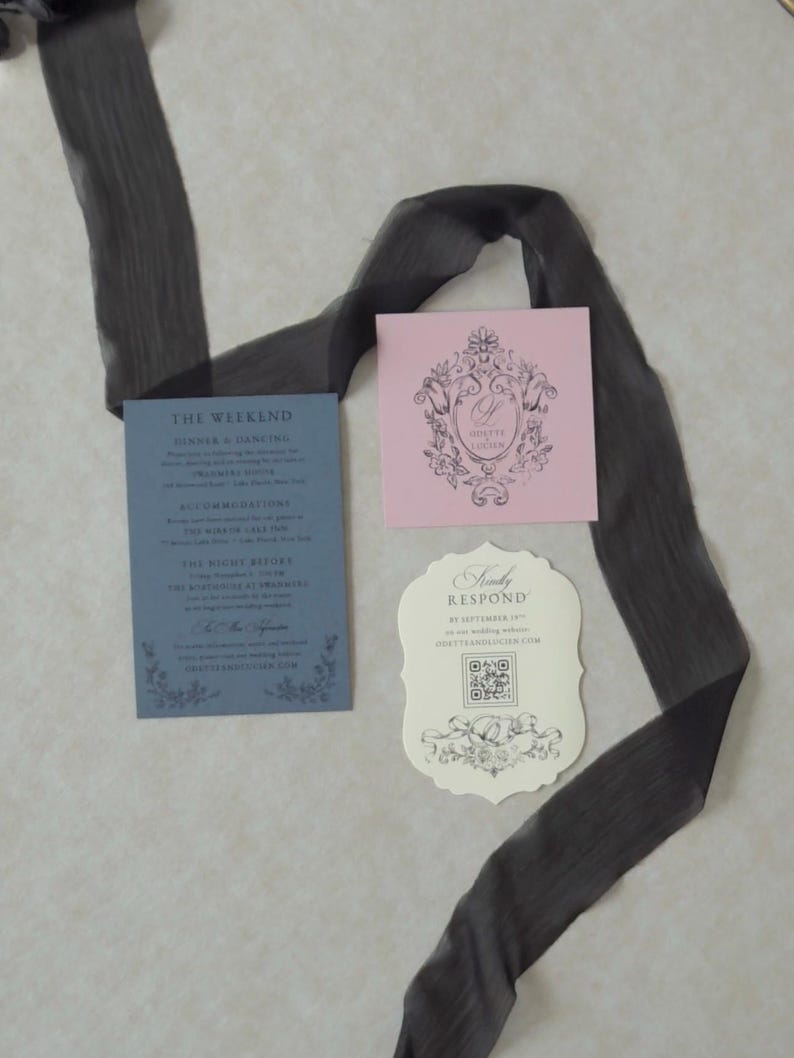 Romantic swan lake wedding stationery with an open Marina blue envelope revealing a dreamy woodland water scene, an ivory botanical invitation, scalloped RSVP card, pink tag, and illustrated vellum jacket.