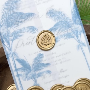 May include: Wedding invitation with a blue palm tree design and gold wax seals. The invitation has the text "Prest" and other details about the event. Several gold wax seals with a leaf design are scattered around the invitation.