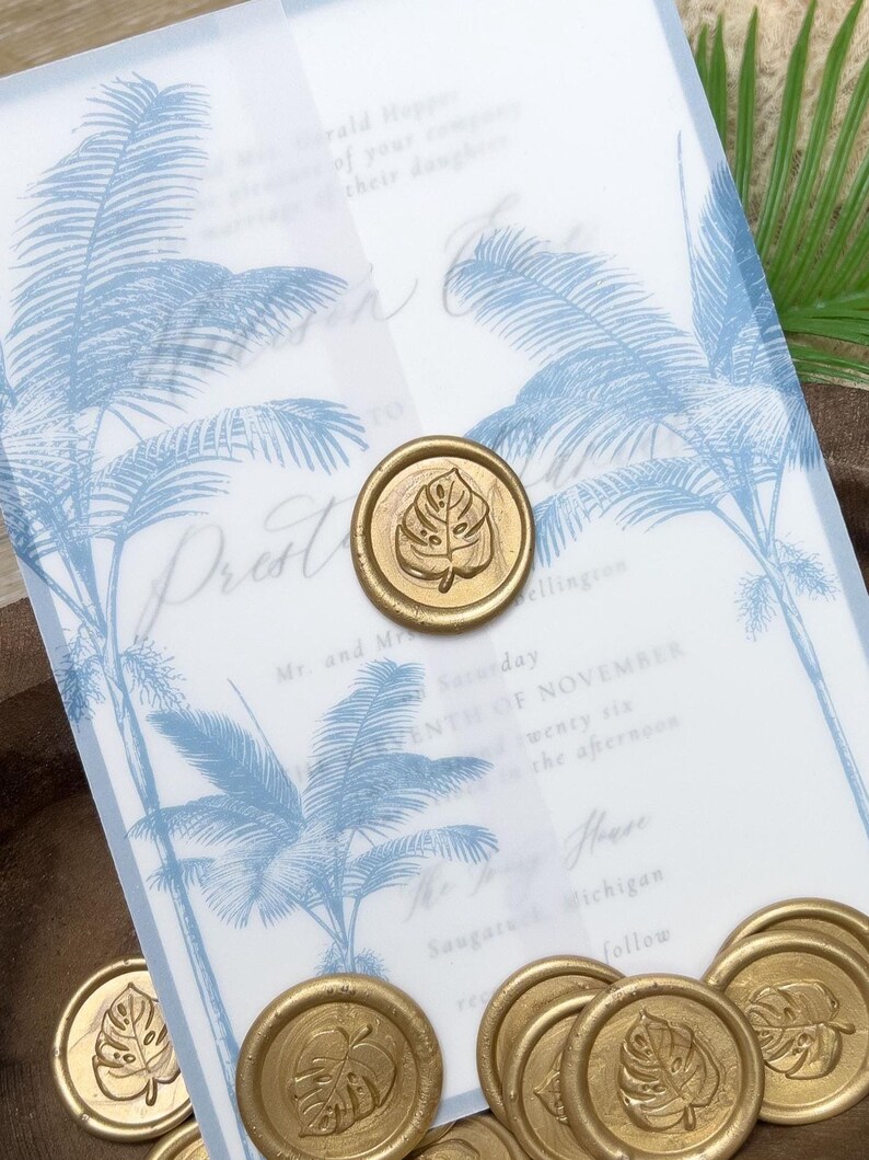 May include: Wedding invitation with a blue palm tree design and gold wax seals. The invitation has the text "Prest" and other details about the event. Several gold wax seals with a leaf design are scattered around the invitation.