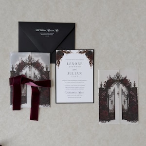 Gothic floral wedding invitation featuring a white invitation with elegant typography, black backing mat, translucent vellum jacket printed with ornate castle gates and burgundy roses, and coordinating dark romantic stationery.