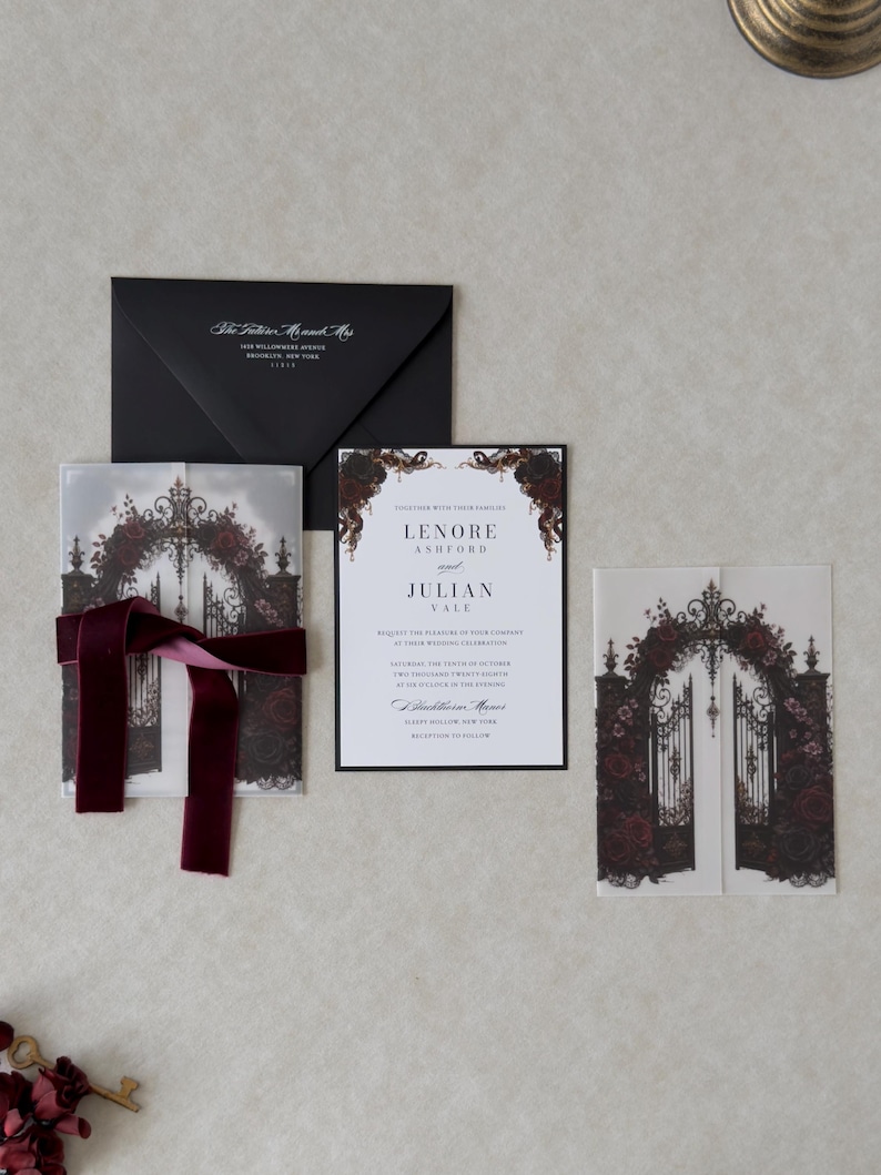 Gothic floral wedding invitation featuring a white invitation with elegant typography, black backing mat, translucent vellum jacket printed with ornate castle gates and burgundy roses, and coordinating dark romantic stationery.