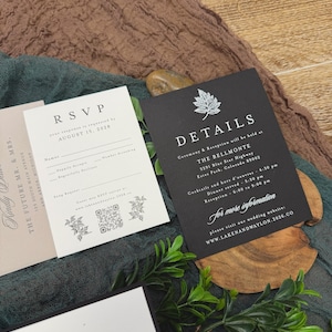 May include: A collection of wedding stationery, including RSVP and details cards, with elegant typography. The cards are in black and white, with floral accents. The background features a textured brown and green fabric.