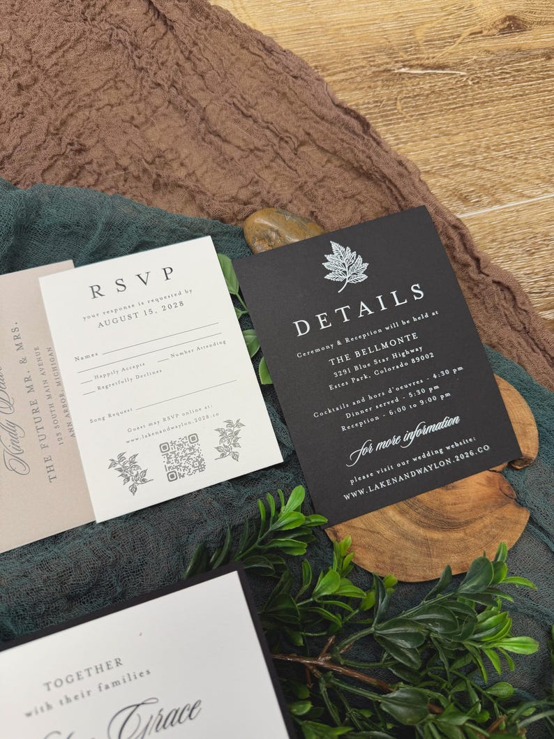 May include: A collection of wedding stationery, including RSVP and details cards, with elegant typography. The cards are in black and white, with floral accents. The background features a textured brown and green fabric.