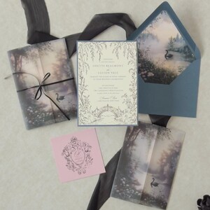 Odette romantic fairytale wedding stationery arranged on a neutral backdrop with a botanical ivory invitation, Marina blue details card, scalloped RSVP, Dusk pink decorative tag, misty forest vellum jacket, and swan lake envelope liner.