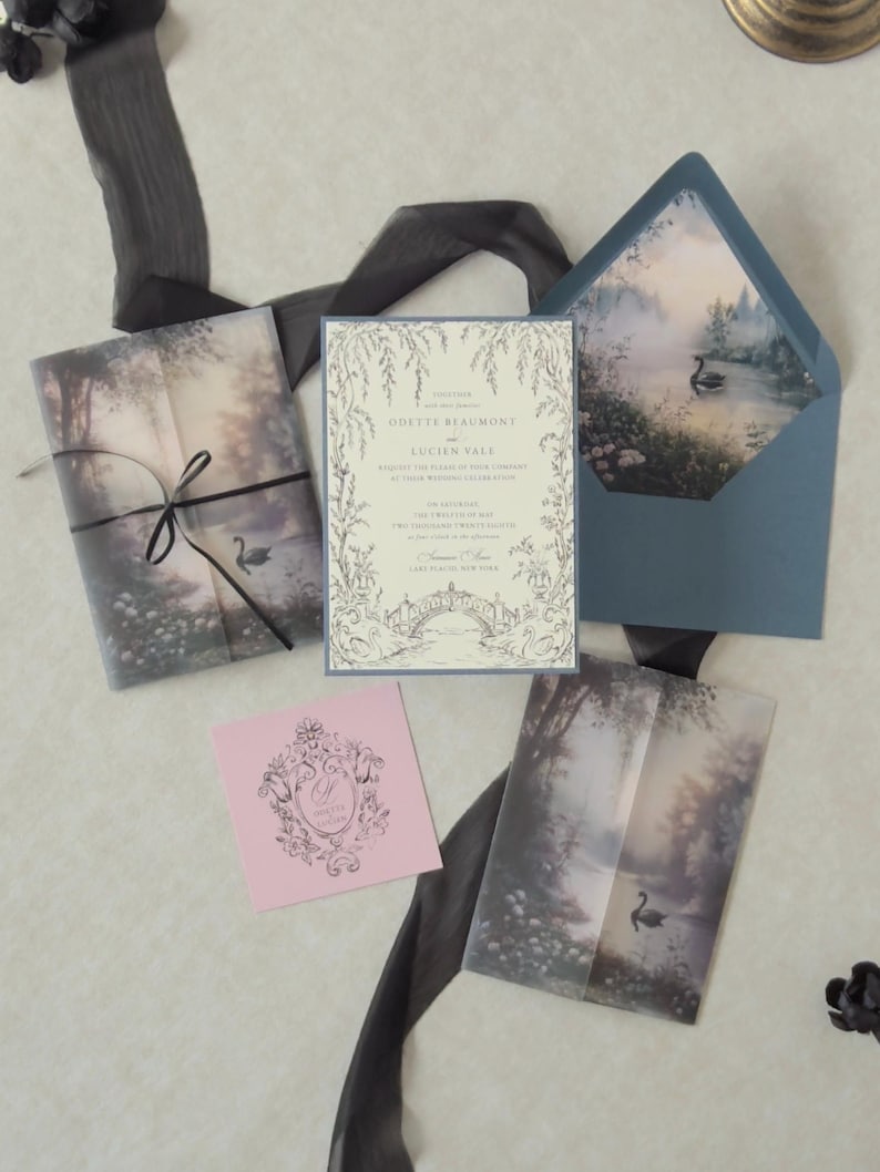 Odette romantic fairytale wedding stationery arranged on a neutral backdrop with a botanical ivory invitation, Marina blue details card, scalloped RSVP, Dusk pink decorative tag, misty forest vellum jacket, and swan lake envelope liner.
