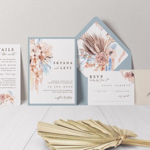 May include: Wedding invitation suite with a dusty blue envelope, a white invitation card with a floral design, and a white RSVP card. The invitation card features the text "Skyana and Levi" and the date "10 Jul 2023".