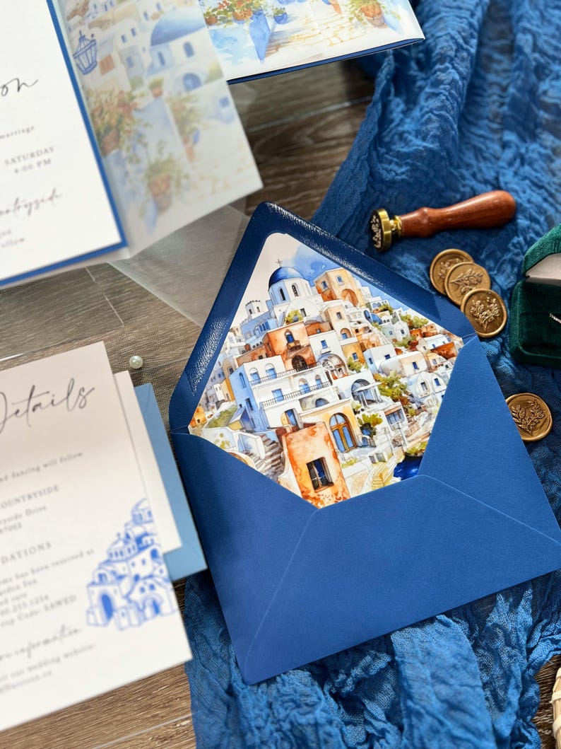 May include: A blue envelope with a watercolor illustration of a white and blue Greek village on the front. The envelope is decorated with a wax seal.