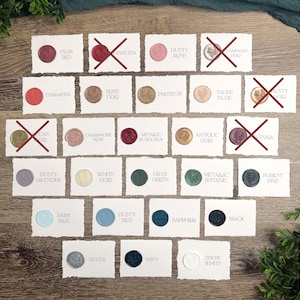 May include: A collection of rectangular white paper cards with deckled edges, each featuring a circular wax seal with a floral design. The seals are in various colors including red, pink, gold, green, blue, and white, with text labels identifying each color.