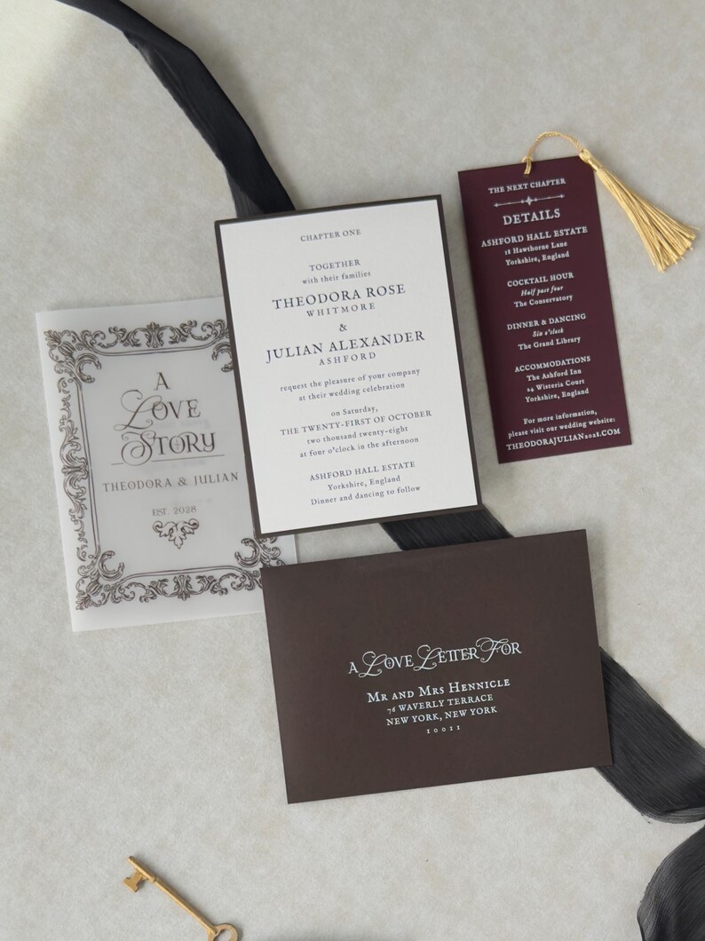 Romantic dark academia wedding stationery with an ivory invitation, burgundy bookmark with gold tassel, ornate decorative card, and coordinating dark envelope, featuring a vintage literary wedding aesthetic.