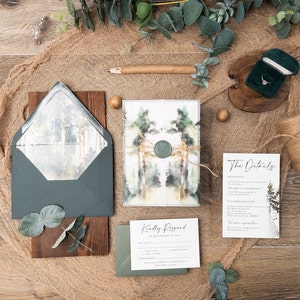 May include: A wedding invitation suite featuring a watercolour forest design. The invitation includes a green and brown envelope with a wax seal. The RSVP card has a green envelope and the details card features a watercolour forest design.