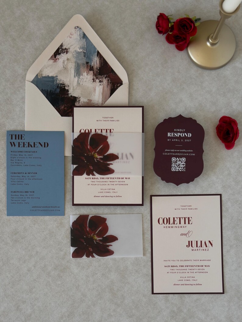 Burgundy, blush and dusty blue wedding stationery arranged in a layered flat lay, featuring a floral wedding invitation, scalloped RSVP card and coordinating details card with rich romantic colors.