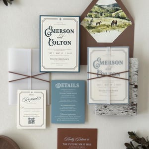 Western-inspired Emerson wedding invitation suite featuring an ivory invitation with vintage typography, dusty blue details card, square RSVP card, warm brown envelope and scenic ranch landscape liner.
