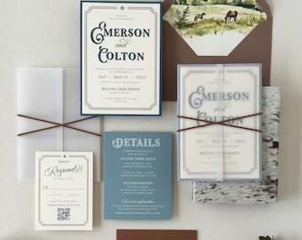 May include: A wedding invitation suite featuring a main card with navy text, a vellum overlay, a blue details card, and a response card with a QR code. The brown envelope has a watercolour landscape liner showing horses in a field. A mailing envelope is included.