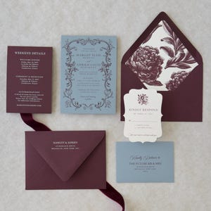 Close-up of premium wedding stationery in dusty blue, burgundy and ivory with scalloped and botanical design details