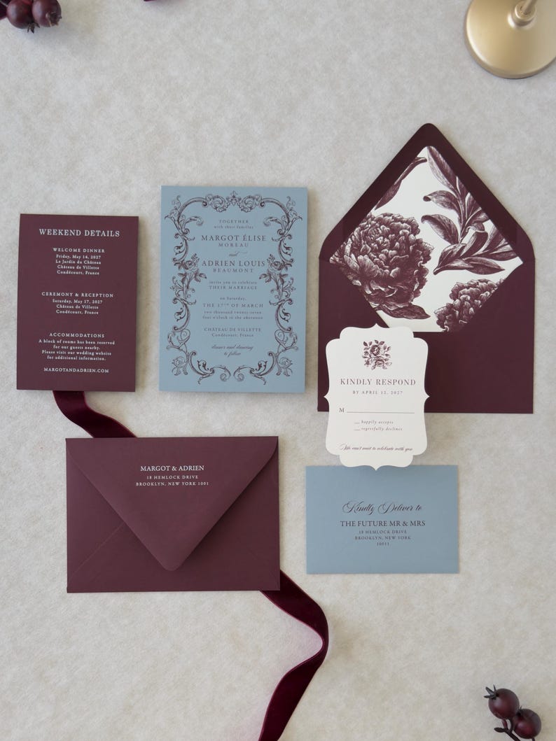 Close-up of premium wedding stationery in dusty blue, burgundy and ivory with scalloped and botanical design details