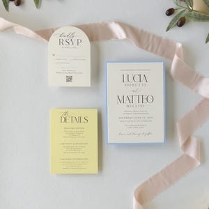 Pale blue layered Lucia wedding invitation paired with butter yellow details card and ivory arch RSVP card, featuring delicate typography and soft pastel colors.