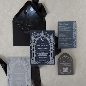 Ophelia dark romantic wedding stationery arranged on a light textured background, featuring a navy blue invitation with white ink Gothic arch artwork, Marina details card, Dark Grey shaped RSVP, printed vellum jacket, and Ebony envelope with moonlit liner.