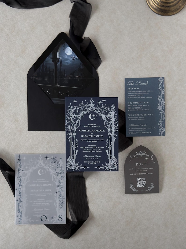 Ophelia dark romantic wedding stationery arranged on a light textured background, featuring a navy blue invitation with white ink Gothic arch artwork, Marina details card, Dark Grey shaped RSVP, printed vellum jacket, and Ebony envelope with moonlit liner.