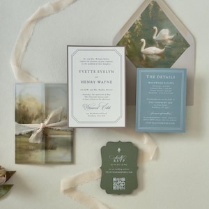 Ivory Yvette wedding invitation paired with dusty blue details card and dark green scalloped RSVP card, displayed with a soft countryside vellum wrap and swan-lined envelope.