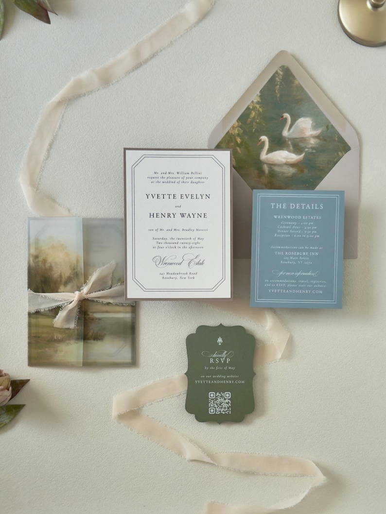 Ivory Yvette wedding invitation paired with dusty blue details card and dark green scalloped RSVP card, displayed with a soft countryside vellum wrap and swan-lined envelope.