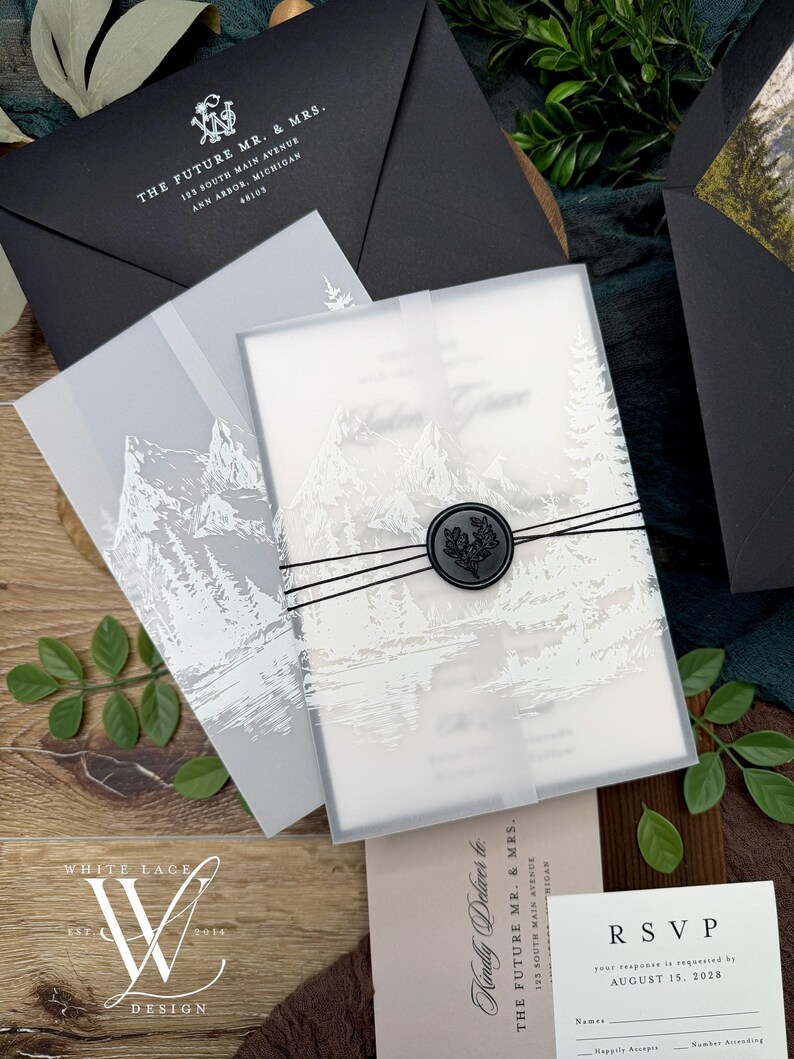 May include: Elegant wedding invitation suite featuring a frosted invitation with a mountain scene, sealed with a black wax stamp. Includes black envelopes and RSVP cards. The suite is tied with black twine and includes the text "THE FUTURE MR. & MRS."