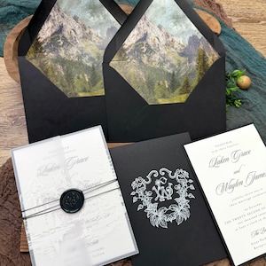 May include: Elegant wedding invitation suite featuring black envelopes with mountain scene liners, a vellum wrap with a wax seal, and invitation cards with floral and monogram designs. The suite includes invitation cards with the names "Laken Grace" and "Waylon James".