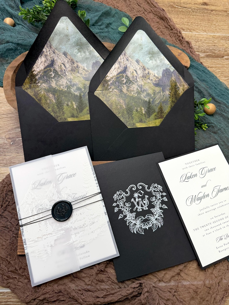 May include: Elegant wedding invitation suite featuring black envelopes with mountain scene liners, a vellum wrap with a wax seal, and invitation cards with floral and monogram designs. The suite includes invitation cards with the names "Laken Grace" and "Waylon James".