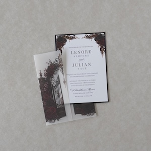White Lenore wedding invitation featuring refined serif typography and romantic Gothic styling, displayed over dark floral vellum artwork on a neutral textured background.