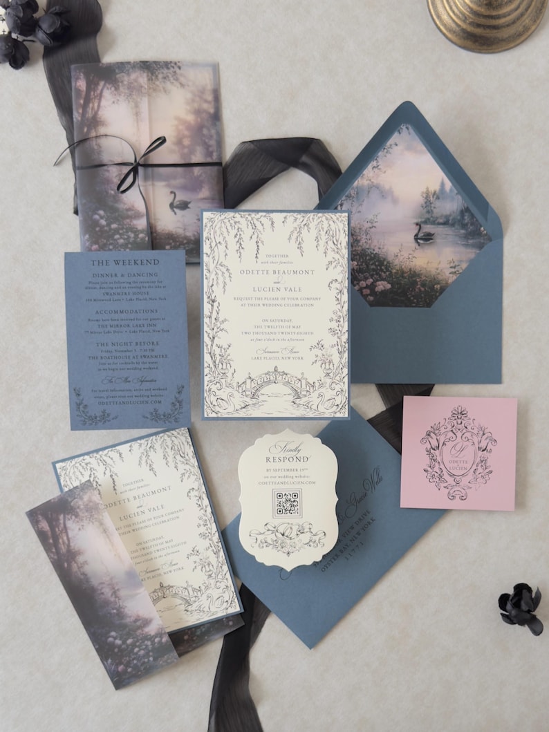 Odette enchanted swan lake wedding invitation suite featuring a Cloud Ivory invitation with Marina blue backing mat, illustrated misty woodland vellum jacket tied with black ribbon, Marina details card, scalloped RSVP, Dusk pink tag, and blue envelope with a romantic swan lake liner.