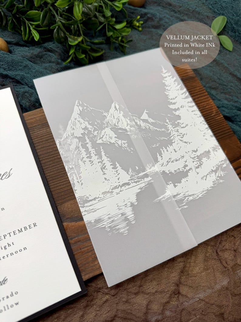 May include: A vellum jacket with a white mountain and forest design, printed in white ink. The jacket is part of a wedding invitation suite. The text on the jacket reads "VELLUM JACKET Printed in White Ink Included in all suites!"