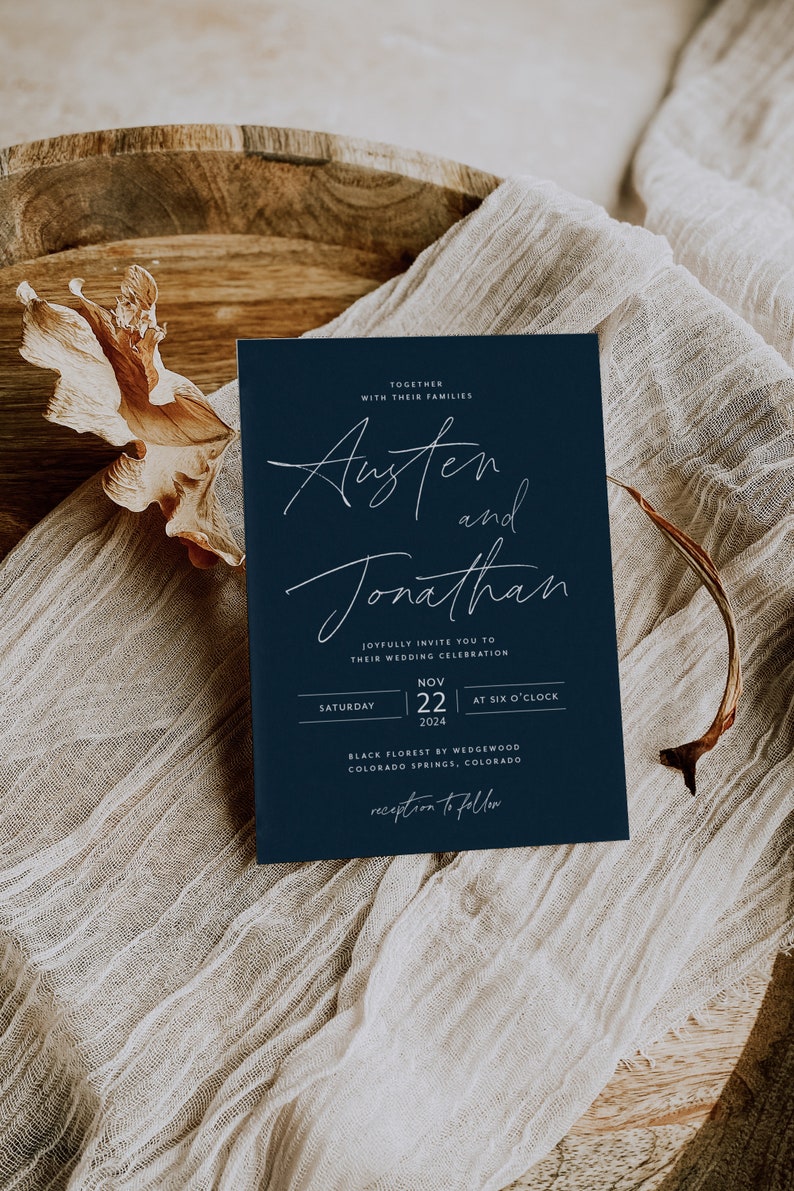 May include: A navy blue wedding invitation with white calligraphy for Austen and Jonathan. The invitation details the wedding date, time, and location: Saturday, November 22, 2024, at six o'clock, Black Florest by Wedgewood, Colorado Springs, Colorado. The invitation also includes the phrase "reception to follow".