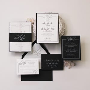 Puede incluir: Un conjunto de invitaciones de boda con papeler&iacute;a en blanco y negro y tipograf&iacute;a serif elegante. El set incluye una invitaci&oacute;n principal, una tarjeta de detalles, una tarjeta RSVP y sobres negros, decorados con un monograma y bordes formales.