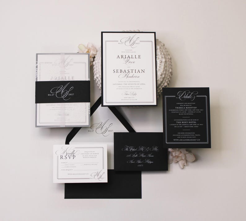 Puede incluir: Un conjunto de invitaciones de boda con papeler&iacute;a en blanco y negro y tipograf&iacute;a serif elegante. El set incluye una invitaci&oacute;n principal, una tarjeta de detalles, una tarjeta RSVP y sobres negros, decorados con un monograma y bordes formales.