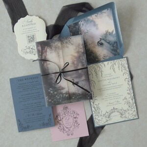 Odette enchanted forest wedding invitation suite featuring a printed lake scene vellum jacket wrapped with black ribbon, accompanied by a romantic botanical invitation, Marina envelope, RSVP card, and Dusk pink tag.