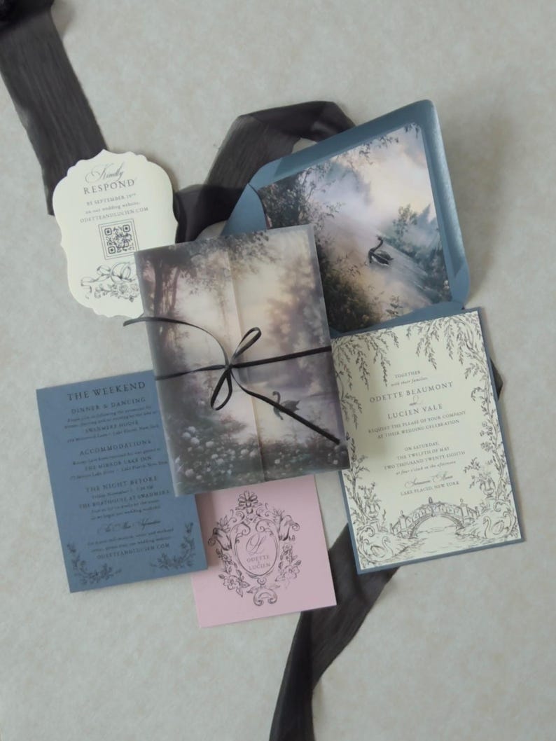 Odette enchanted forest wedding invitation suite featuring a printed lake scene vellum jacket wrapped with black ribbon, accompanied by a romantic botanical invitation, Marina envelope, RSVP card, and Dusk pink tag.