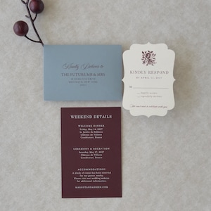 Dusty blue, burgundy and ivory wedding invitation suite styled on a neutral backdrop with romantic botanical details