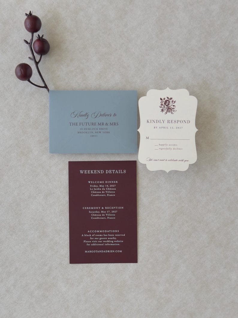 Dusty blue, burgundy and ivory wedding invitation suite styled on a neutral backdrop with romantic botanical details