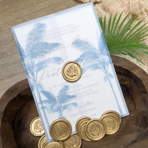 May include: Wedding invitation with blue palm tree design and gold wax seals with leaf imprints. The invitation includes text with wedding details. The seals are scattered in a wooden bowl.