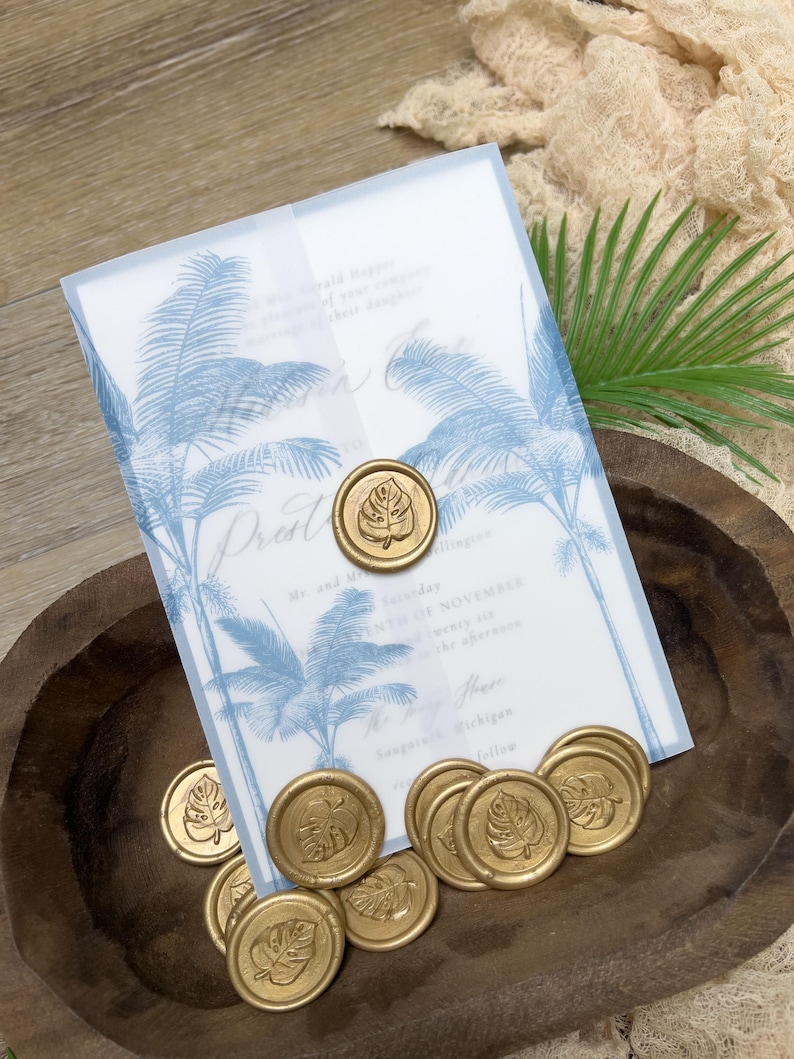 May include: Wedding invitation with blue palm tree design and gold wax seals with leaf imprints. The invitation includes text with wedding details. The seals are scattered in a wooden bowl.