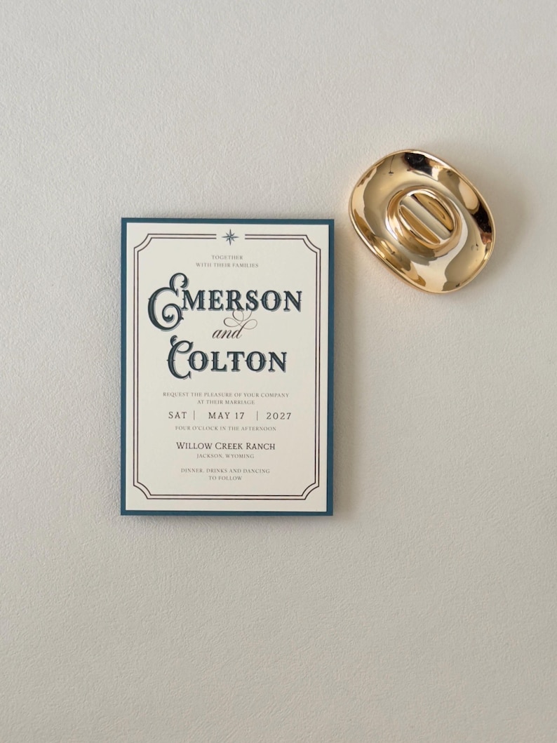Ivory Emerson wedding invitation displayed with a warm brown envelope opened to reveal a scenic green ranch landscape liner and coordinating translucent stationery pieces.
