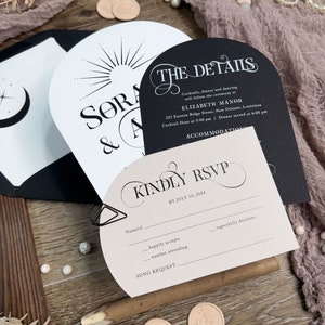 May include: A wedding invitation suite with a black and white design. The invitation features a sunburst design and the text "SORA & A". The details card features the text "THE DETAILS" and includes the wedding date, time, and location. The RSVP card features the text "KINDLY RSVP" and includes a space for guests to RSVP by July 10, 2024.