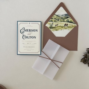 Rustic western wedding stationery featuring an ivory invitation, dusty blue details card, warm brown accents, square RSVP card and coordinating ranch landscape envelope liner.